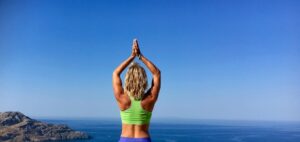 kvinne avbildet bakfra, hun har armene hevet, samlede hender, bakgrunn av hav og himmel