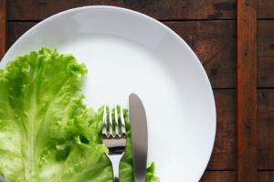 Nært bilde av hvit tallerken med salatblader, kniv og gaffel