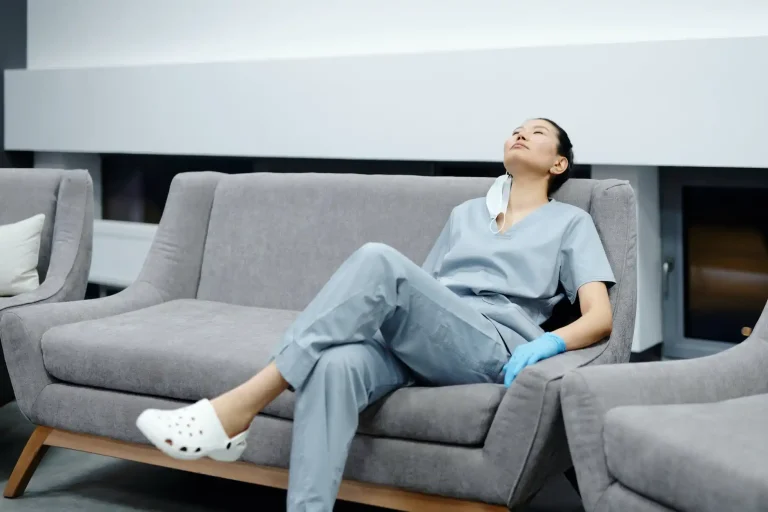 Utslitt sykepleier sitter på en sofa på et sykehus.