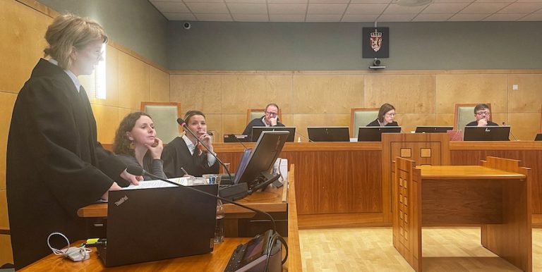 rettssak, dommer i sort kappe foran, bak to kvinner og flere bak skrivebord