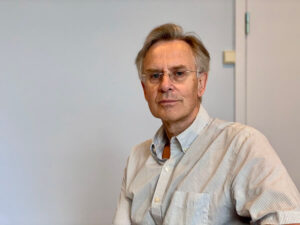 middelaldrende mann med briller og lys skjorte smiler litt mot kamera, grå bakgrunn