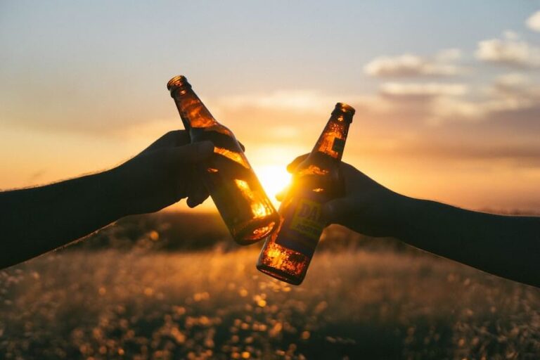 hender som holder en flaske øl hver skåler, solnedgang i bakgrunnen